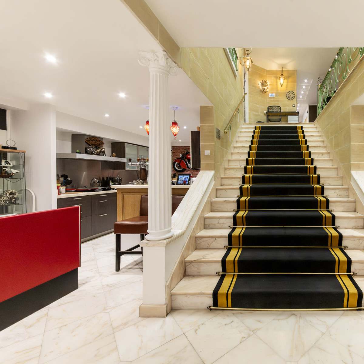 A staircase with a black carpet featuring yellow stripes, leading up to a well-lit upper floor, flanked by two white columns.
