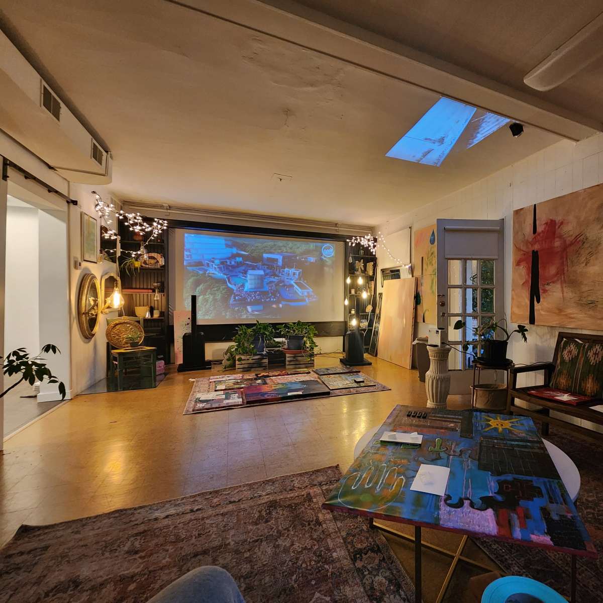 A spacious art studio with colorful artwork displayed on the walls and a large projector screen against one side.