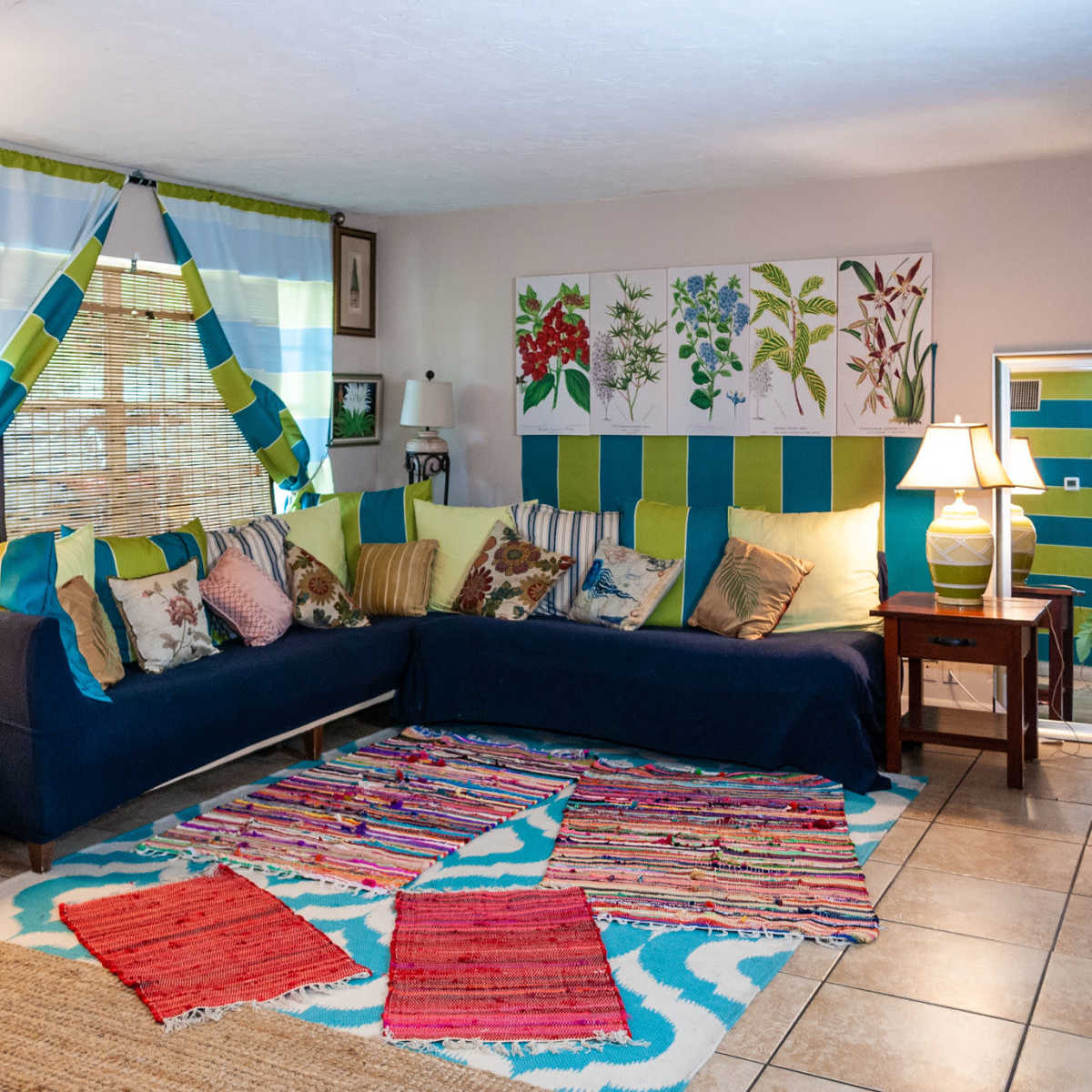 A cozy living room with a sectional couch, colorful pillows, a patterned rug, and decorative artwork on the walls.