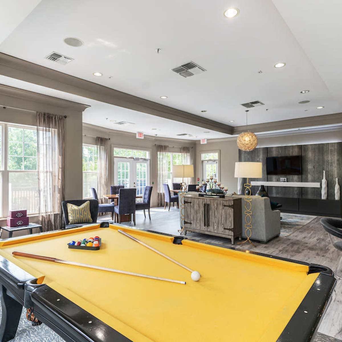 A communal lounge area featuring a billiard table, seating arrangements, and large windows allowing natural light.
