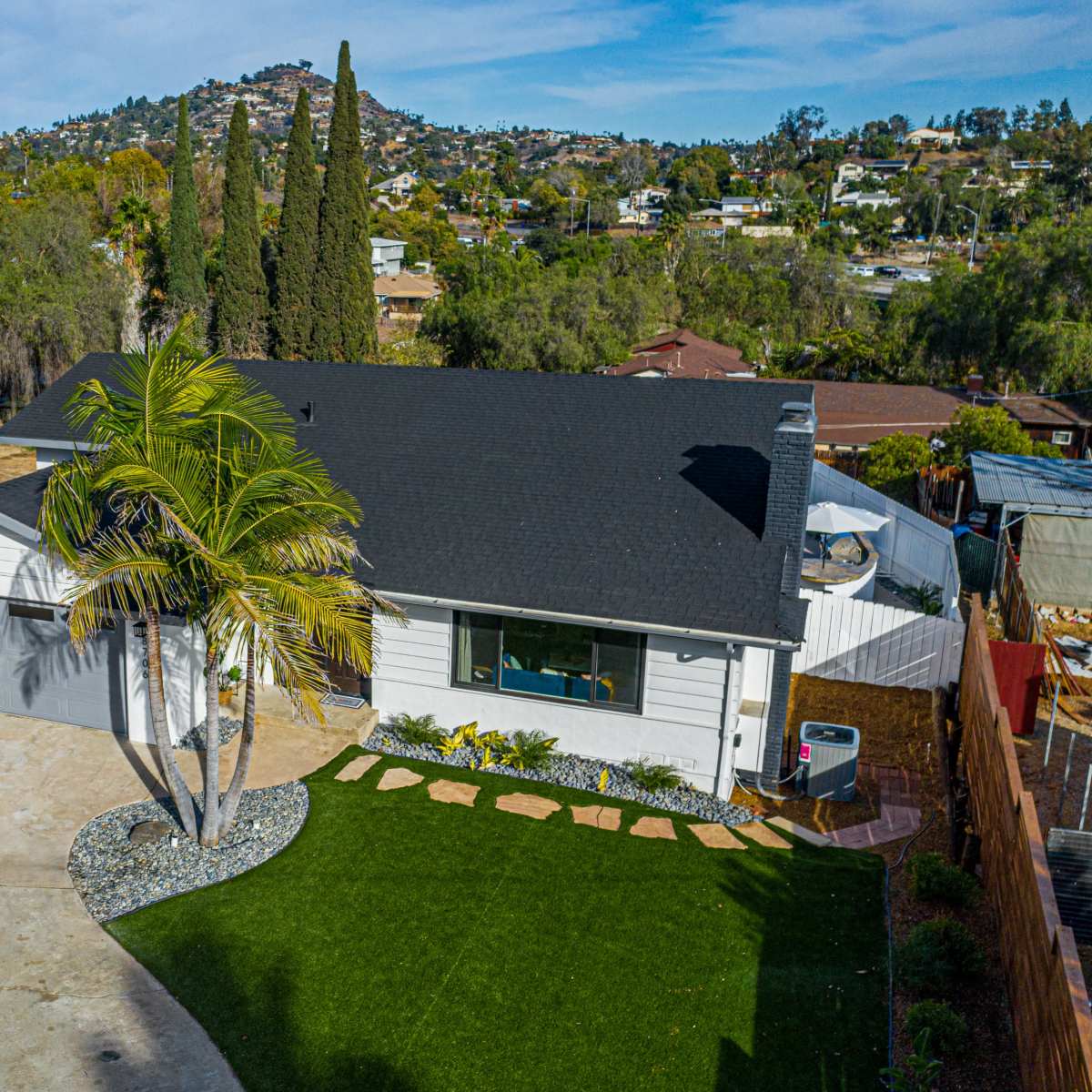 A single-story house with a gray garage sits next to a landscaped yard featuring a palm tree and a concrete driveway.