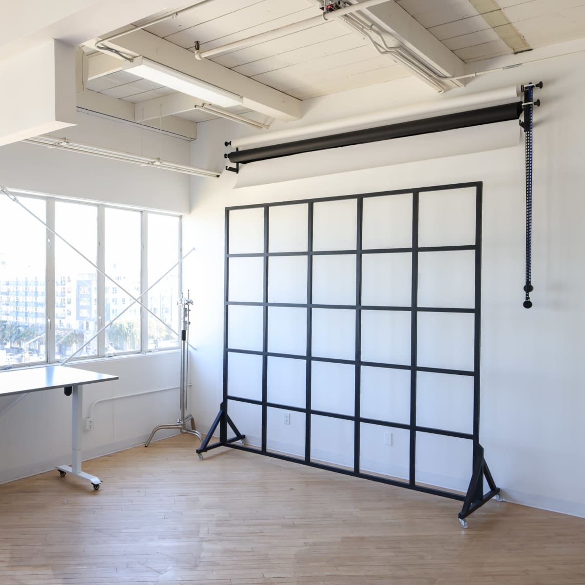 A bright, minimalist studio space featuring a desk and a backdrop setup against a large window.