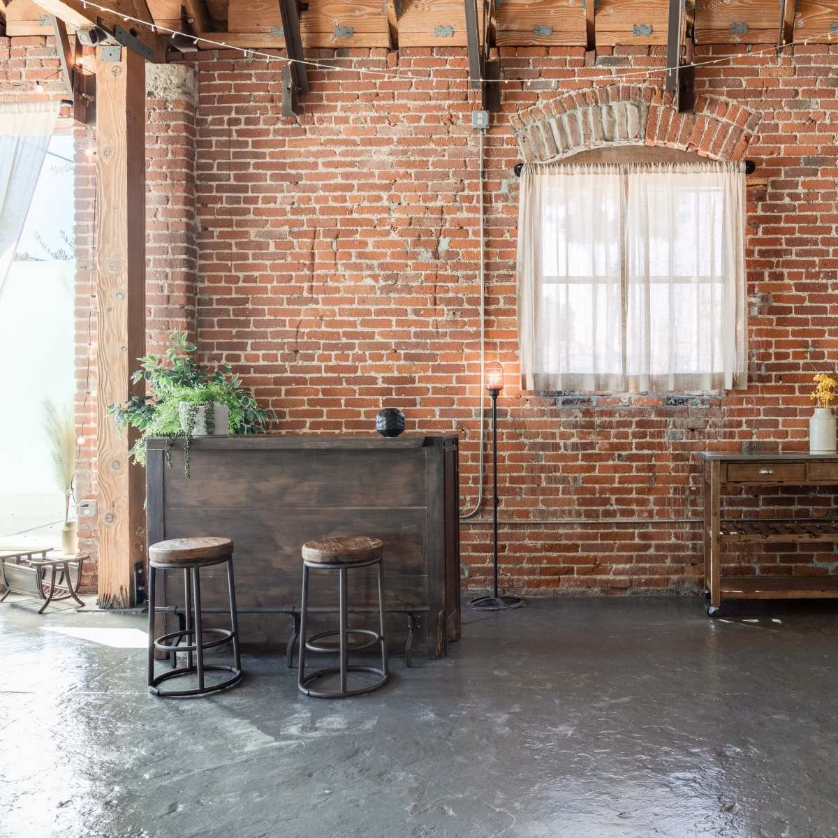 A rustic interior with exposed brick walls, wooden beams, and two bar stools near a wooden counter.