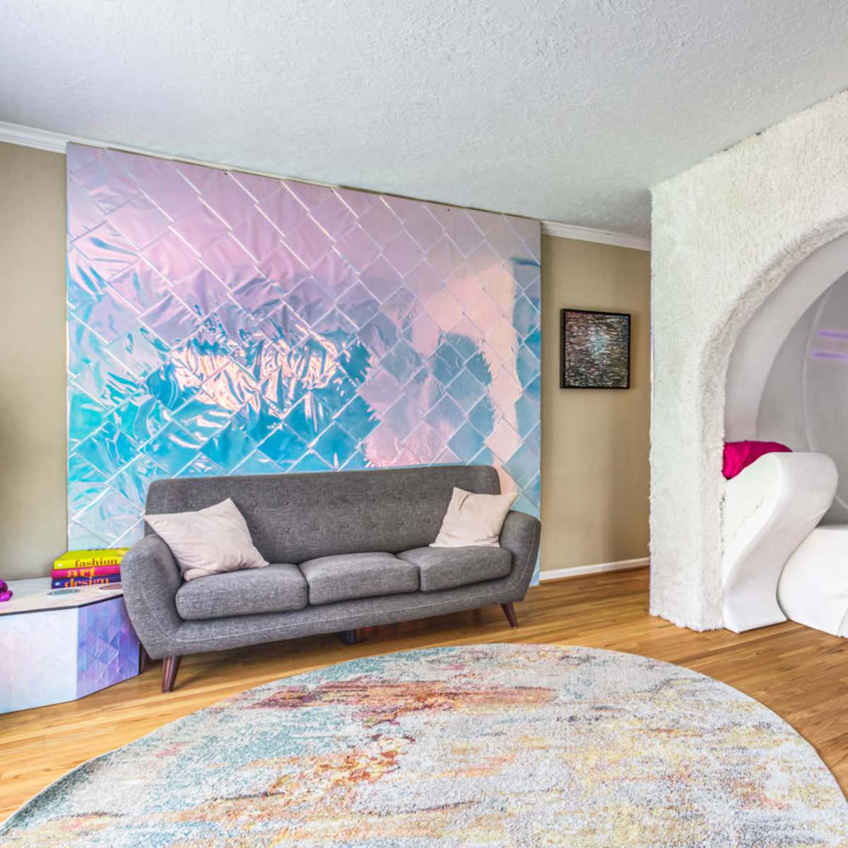 A modern living space featuring a textured wall, a circular rug, a gray sofa, and a unique archway leading to a sculptural seating area.