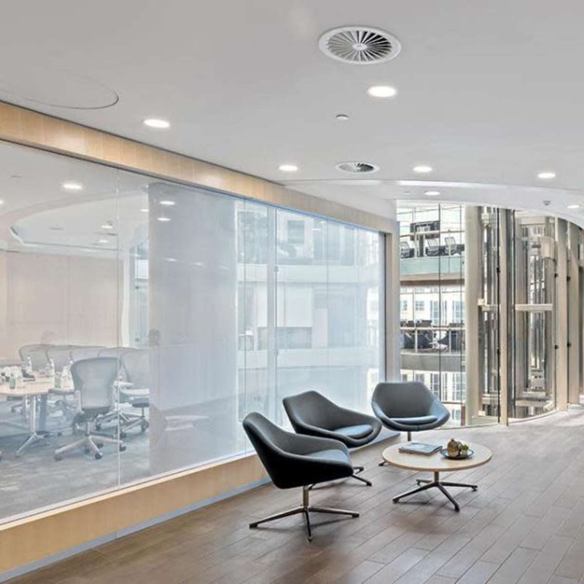 A modern office lobby featuring curved walls, a reception desk, and a glass-walled conference room with seating arrangements.