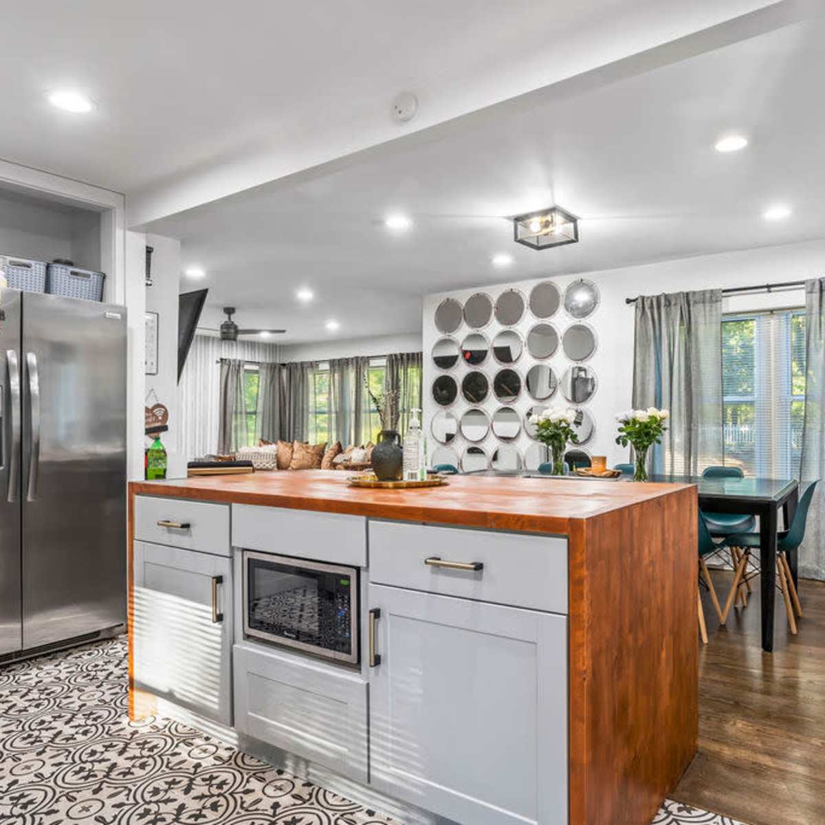 A modern kitchen with a large island featuring a wooden countertop, stainless steel appliances, and decorative wall shelves displaying round metal trays.