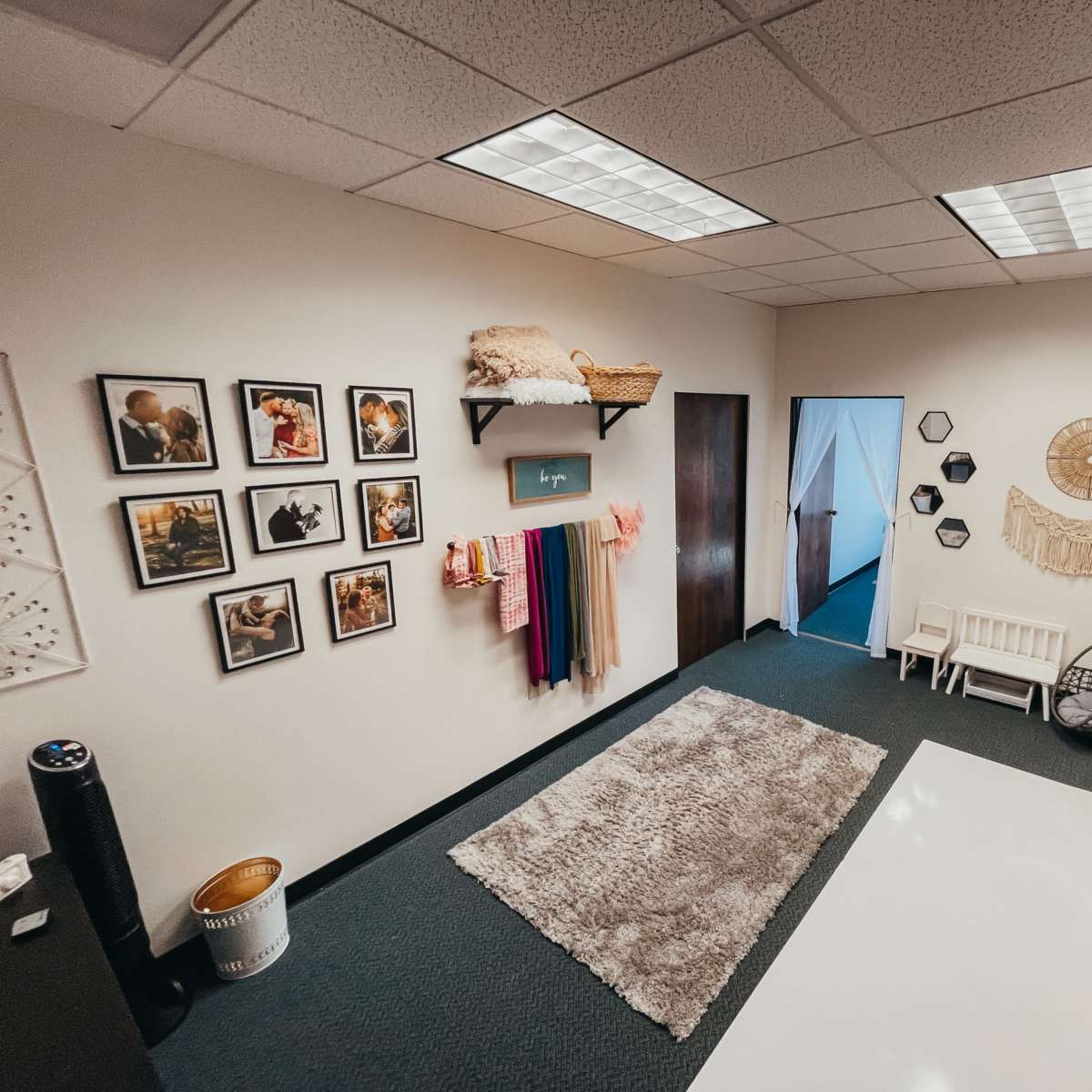 A well-organized interior space featuring framed photographs on the wall, a variety of colorful drapes, a cozy seating area, and decorative wall hangings.