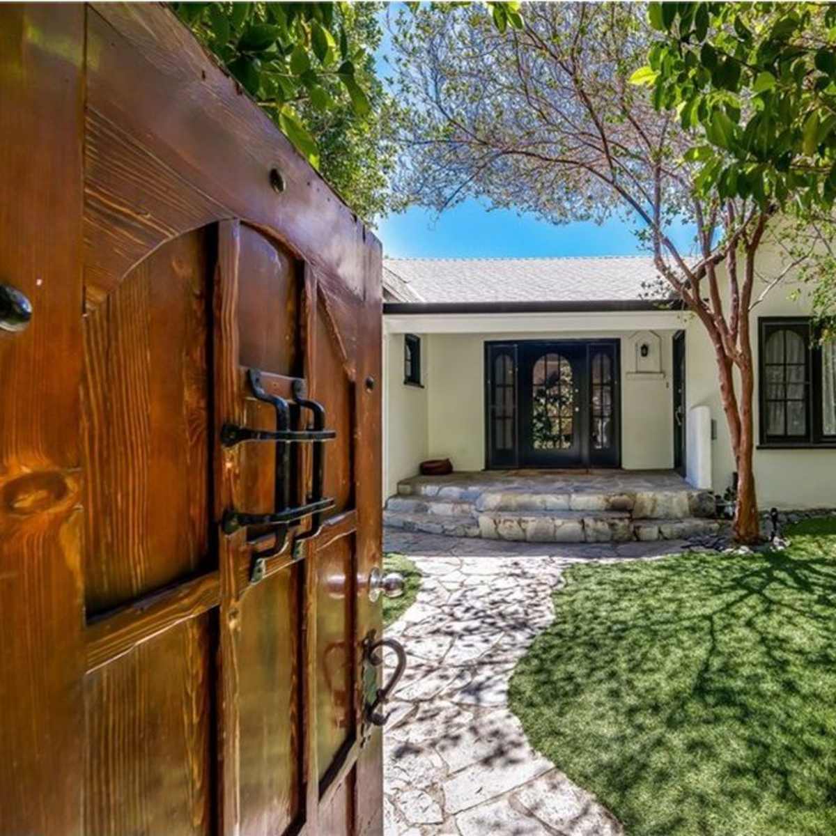 A stone pathway leading to a house with a wooden front door, surrounded by green foliage.