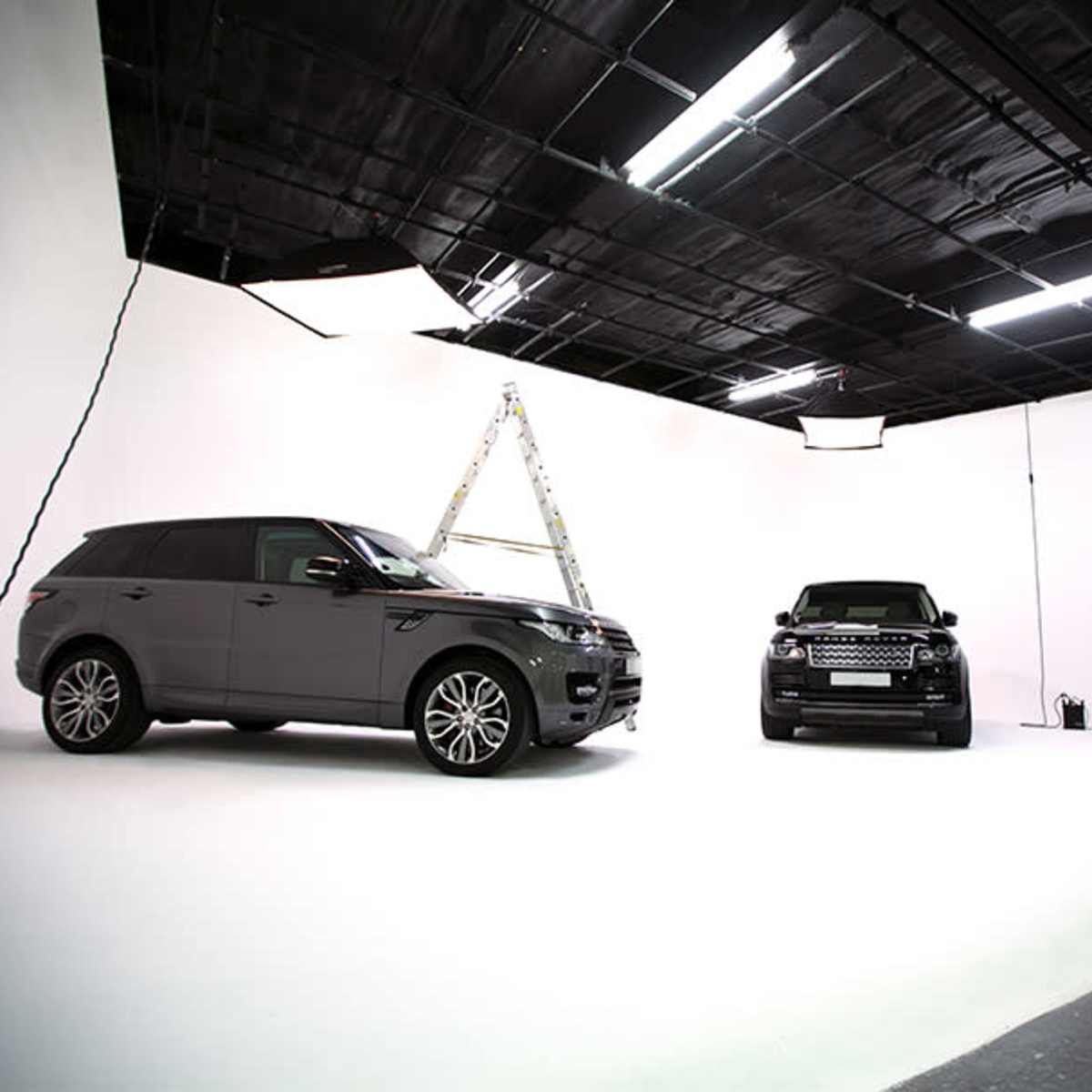Two luxury SUVs parked in a photography studio with a ladder set up in the background.