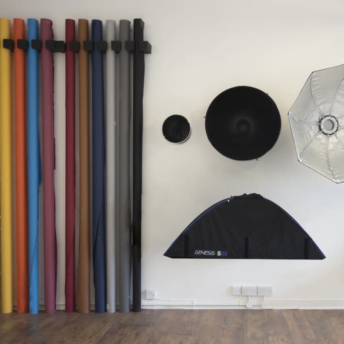 A photography studio setup with a variety of colored backdrop rolls on one side and lighting equipment on the opposite wall, along with an acoustic guitar placed on the floor.