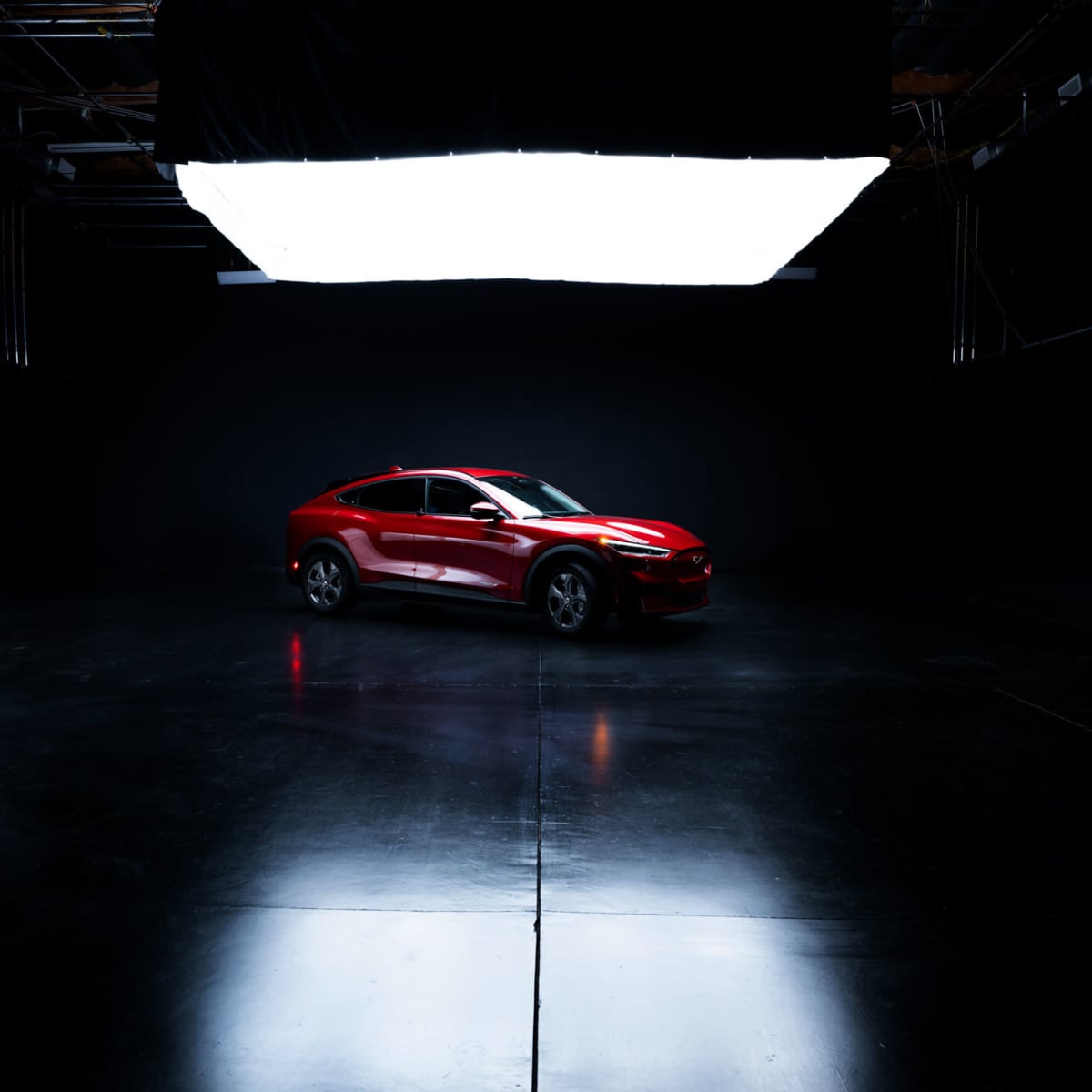 A red car is positioned in a dimly lit studio with a large light source overhead.