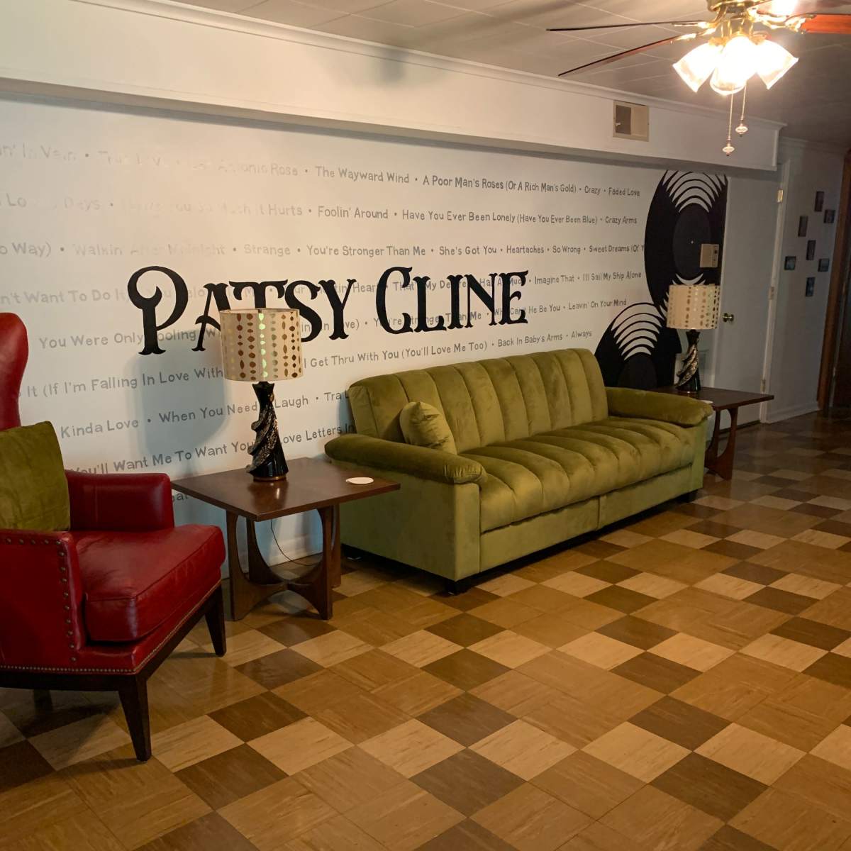 A room with a green couch, a red armchair, and a wall decorated with the name "Patsy Cline" and song lyrics.