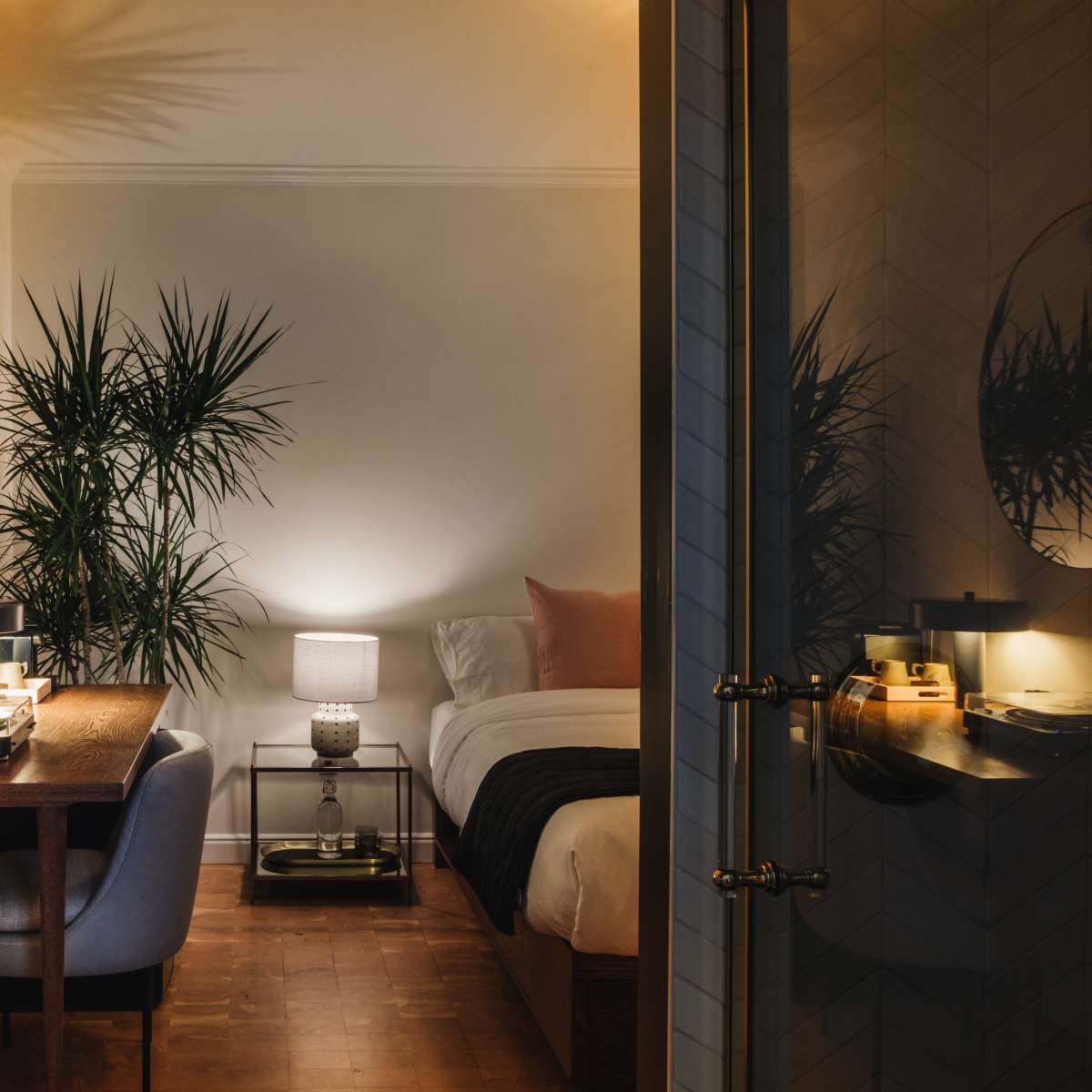 A cozy bedroom features a bed, a desk with a chair, plants, and soft lighting.