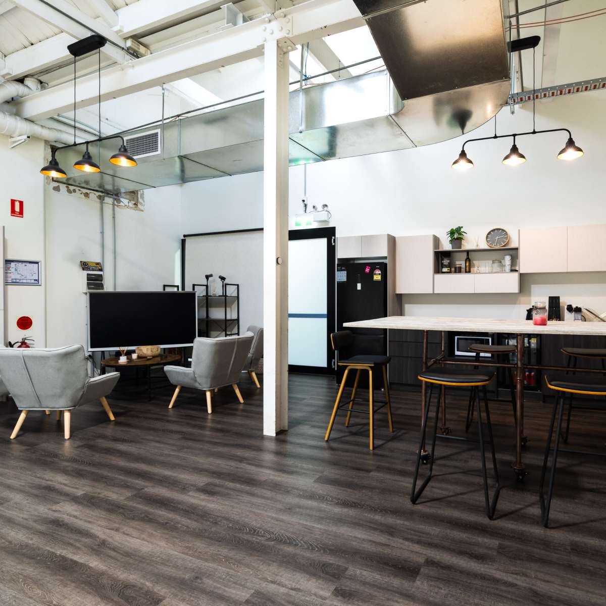 A modern open-plan kitchen and living area with a dining table, chairs, and a television in a bright space.
