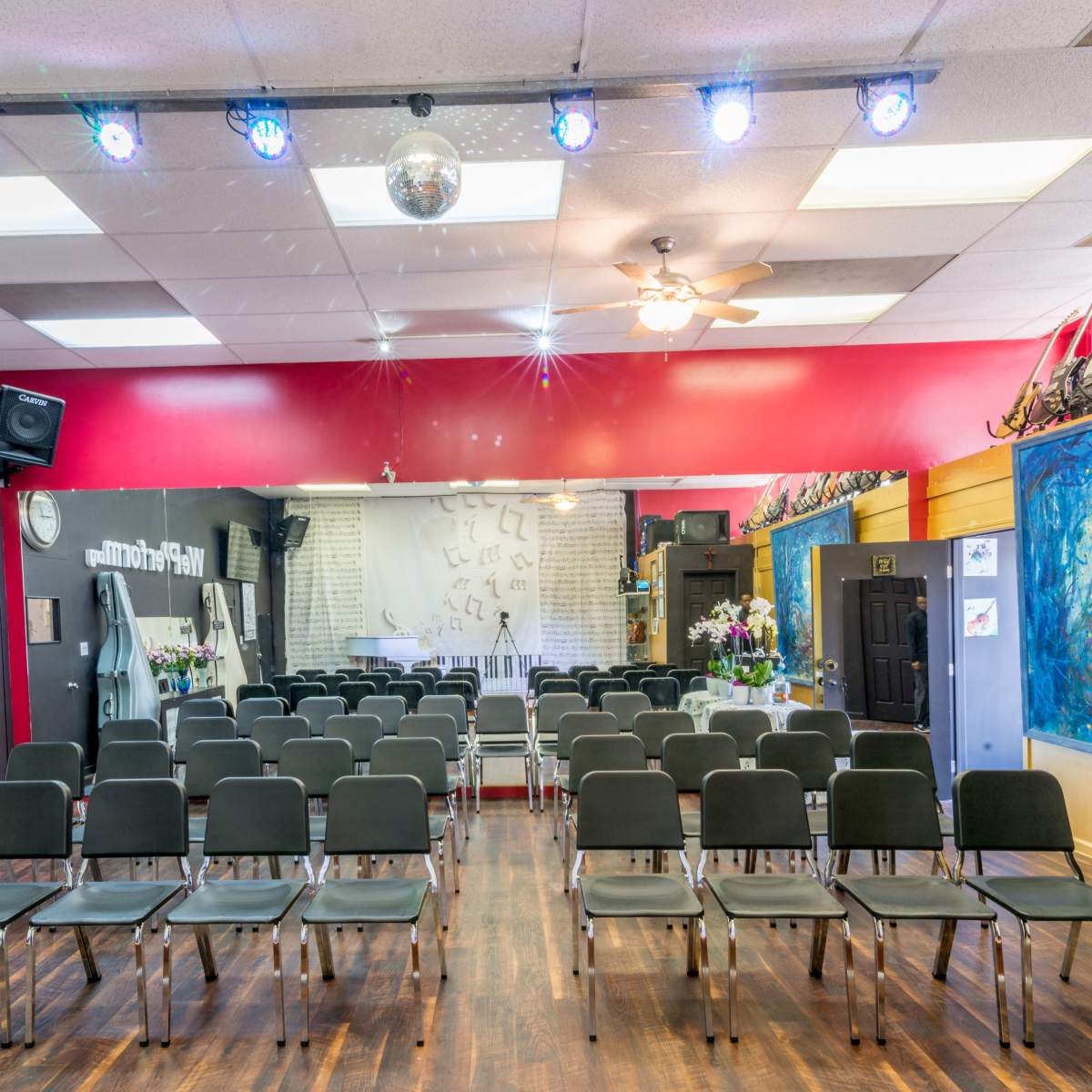 A music performance space arranged with rows of chairs facing a stage, decorated with colorful walls and guitars on display.