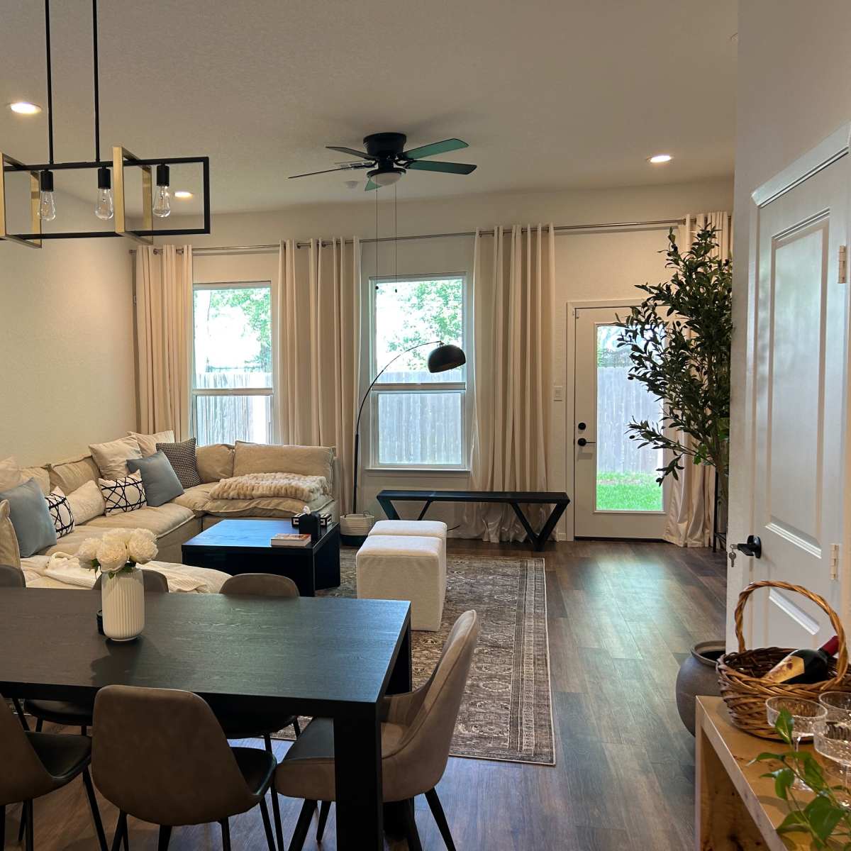 A modern living and dining area featuring a sectional sofa, a dining table with chairs, large windows, and a door leading to an outdoor space.