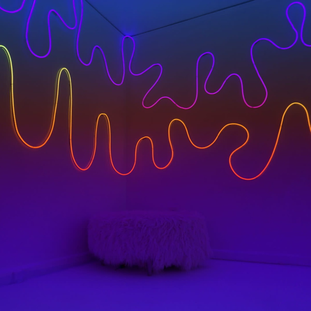 A room with colorful neon light patterns on the walls and a fluffy white seating area in the center.