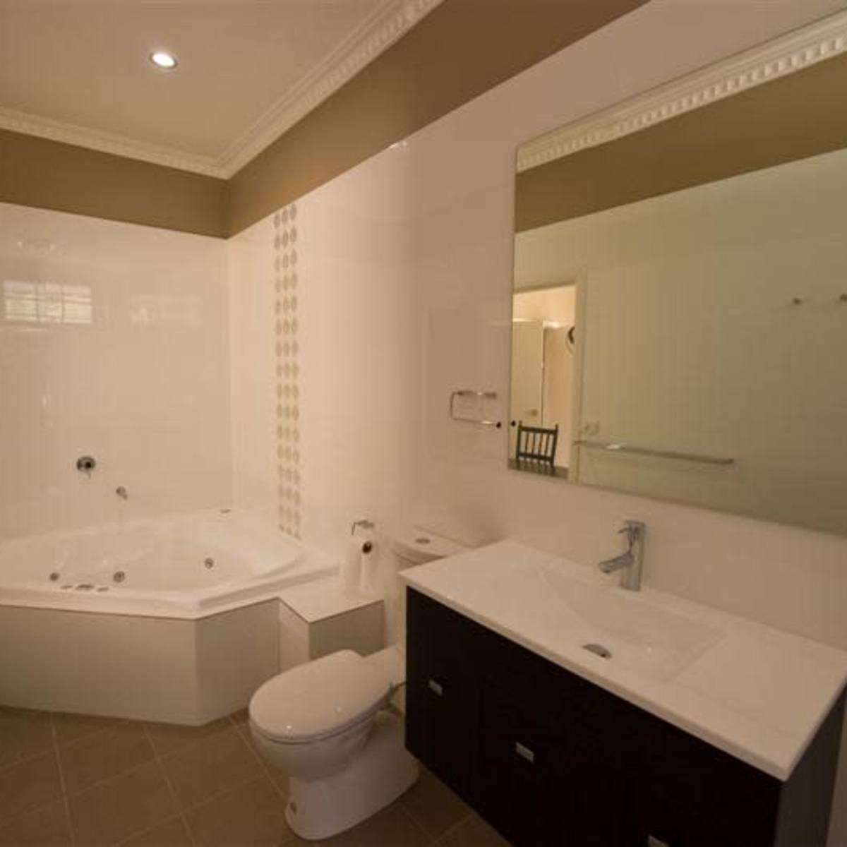 A modern bathroom featuring a jetted bathtub, a wall-mounted mirror, a toilet, and a double sink vanity with dark wood cabinets.