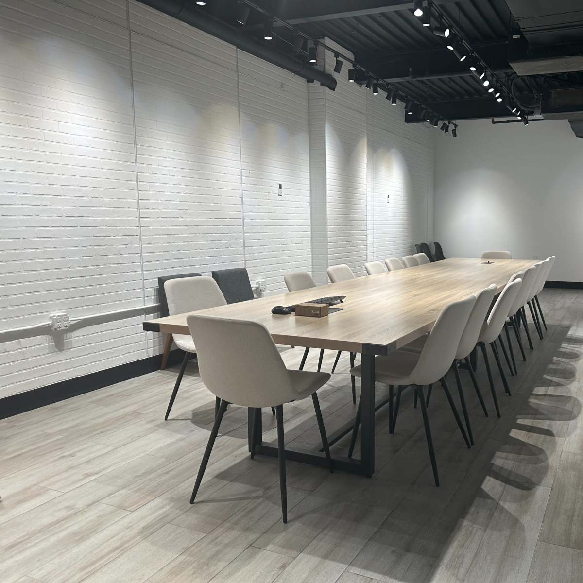 A long wooden conference table is set with chairs along each side in a brightly lit meeting room with white brick walls.