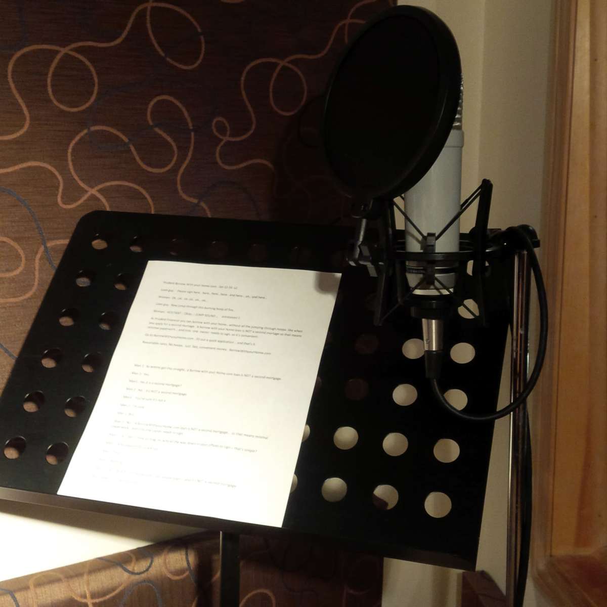 A microphone is positioned next to a music stand holding a sheet of printed text in a recording studio.