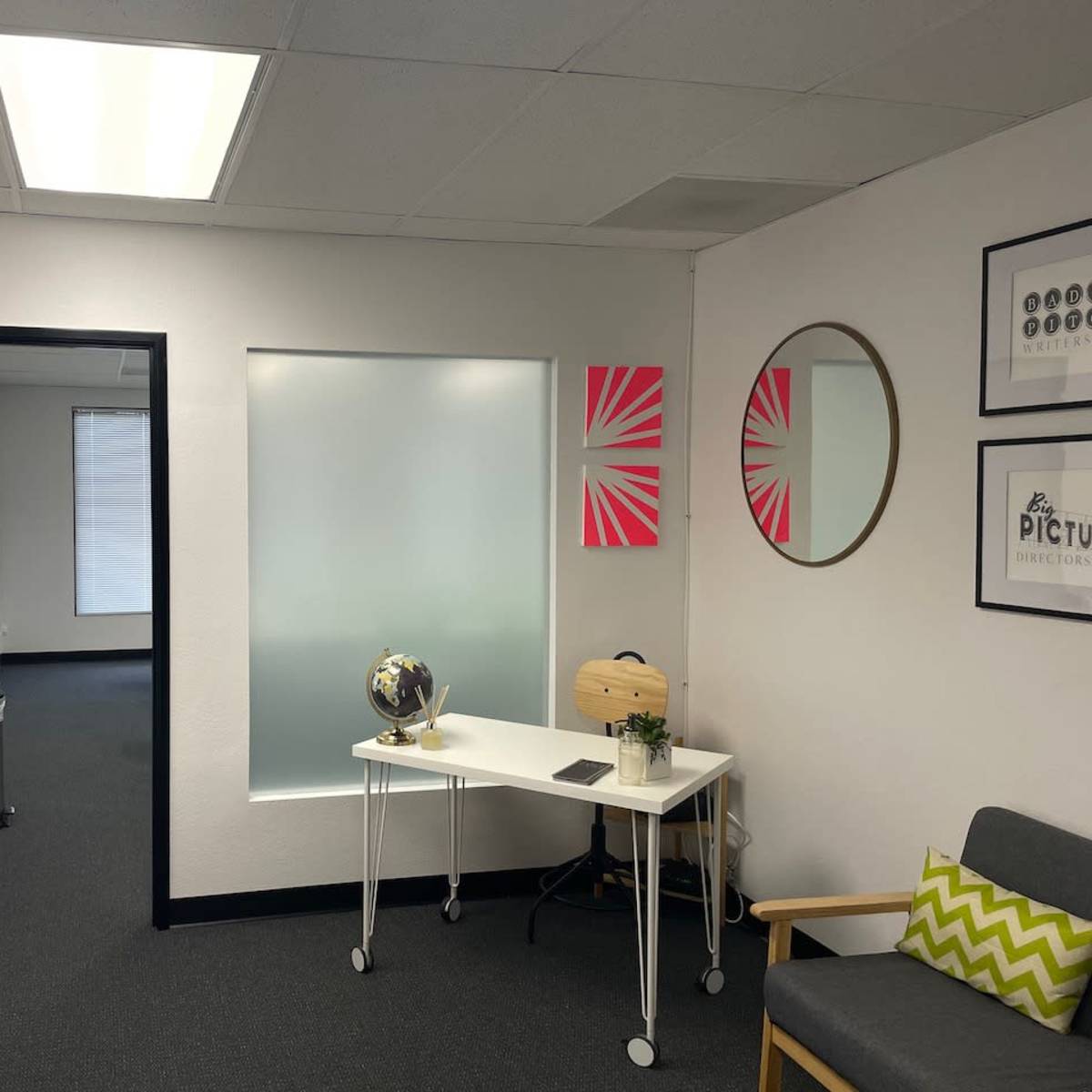 A modern office waiting area with white walls, a desk, a globe, two chairs, and bright wall decorations.