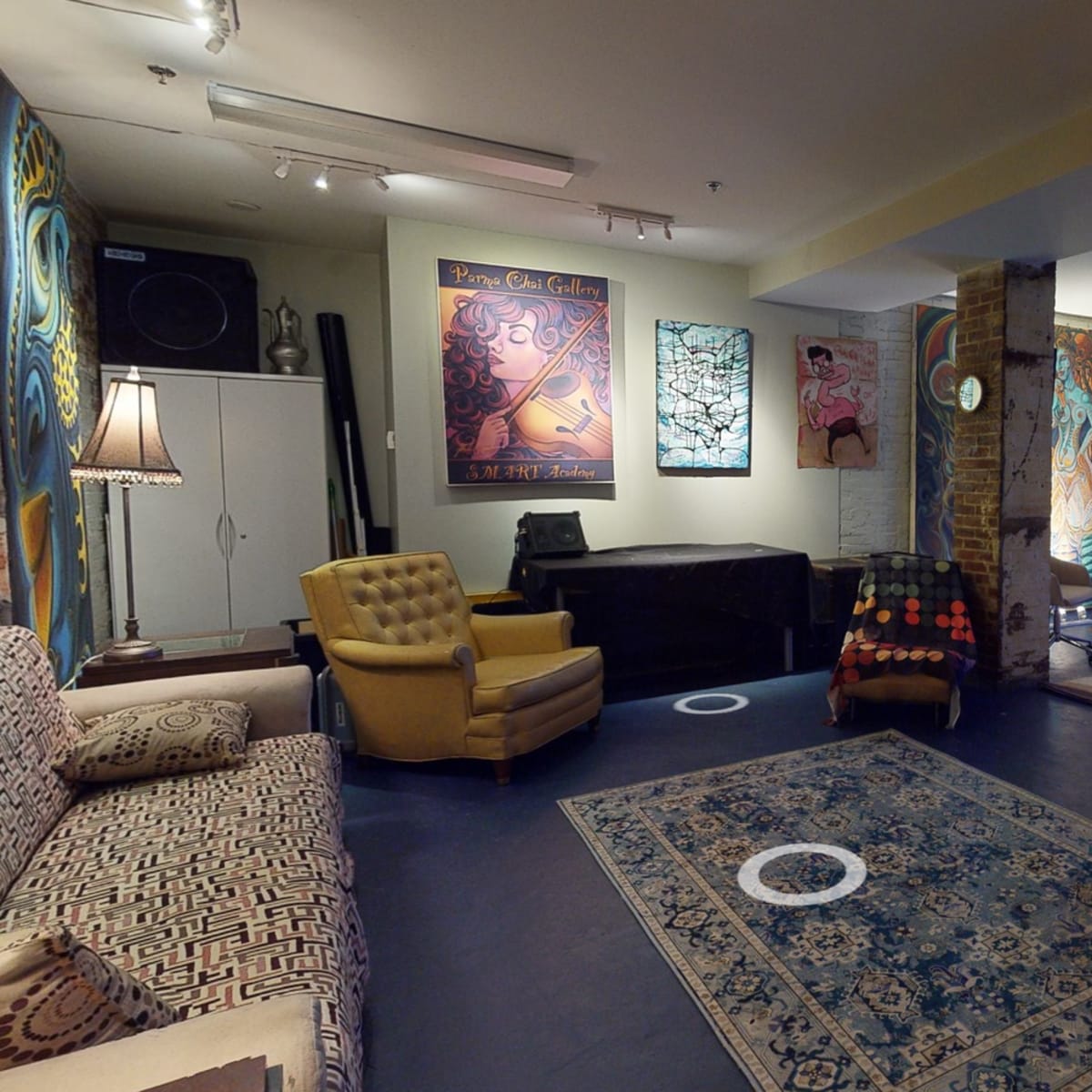 A spacious art studio or gallery with various artworks displayed on the walls, patterned rugs on the floor, and a mix of seating arrangements.
