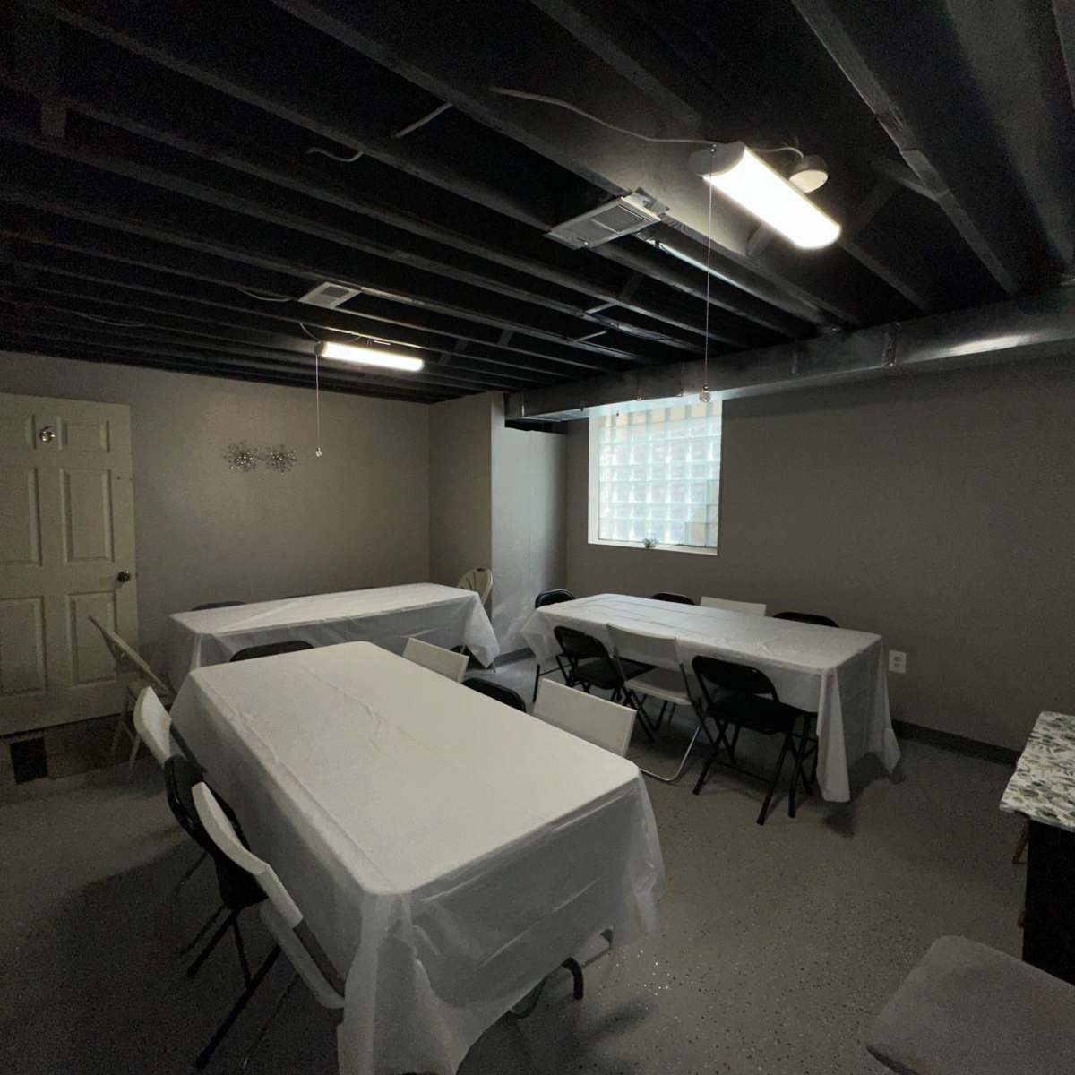 A basement room with several tables covered in white cloths and a window on one wall.