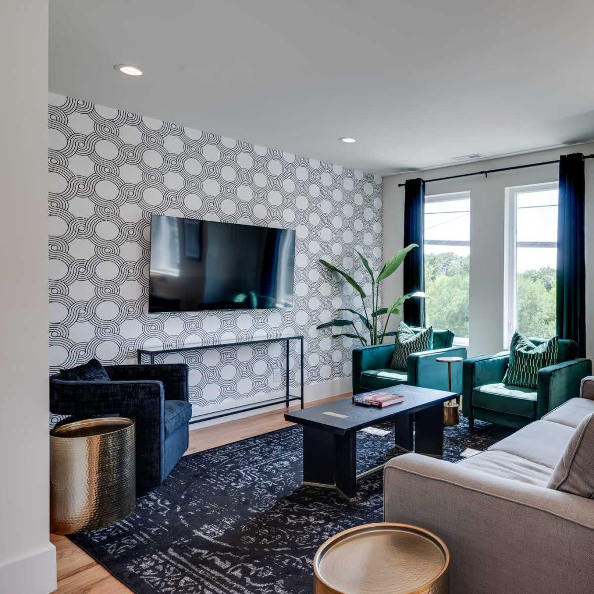 The living room features a modern design with a large television, seating arrangements including a gray sofa and green chairs, and a patterned wall.