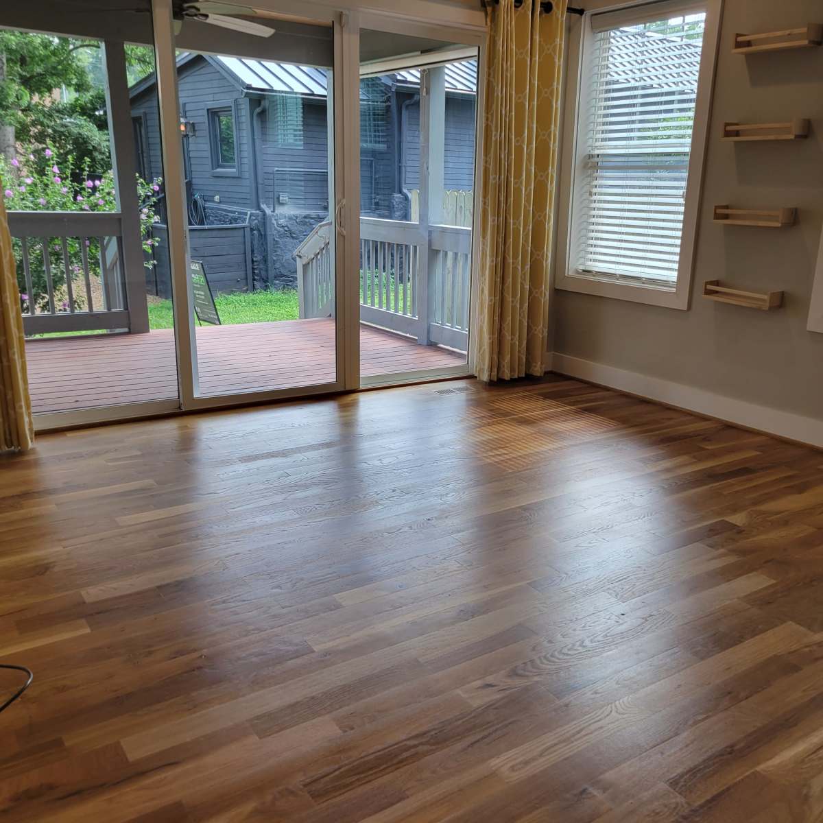 A living room with hardwood flooring, large windows, and a sliding glass door leading to a deck and backyard.