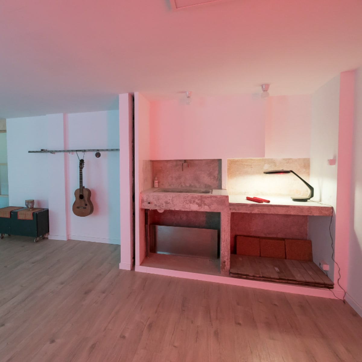 A spacious, modern room with wooden flooring, a concrete countertop, a lamp, and a guitar hanging on the wall.