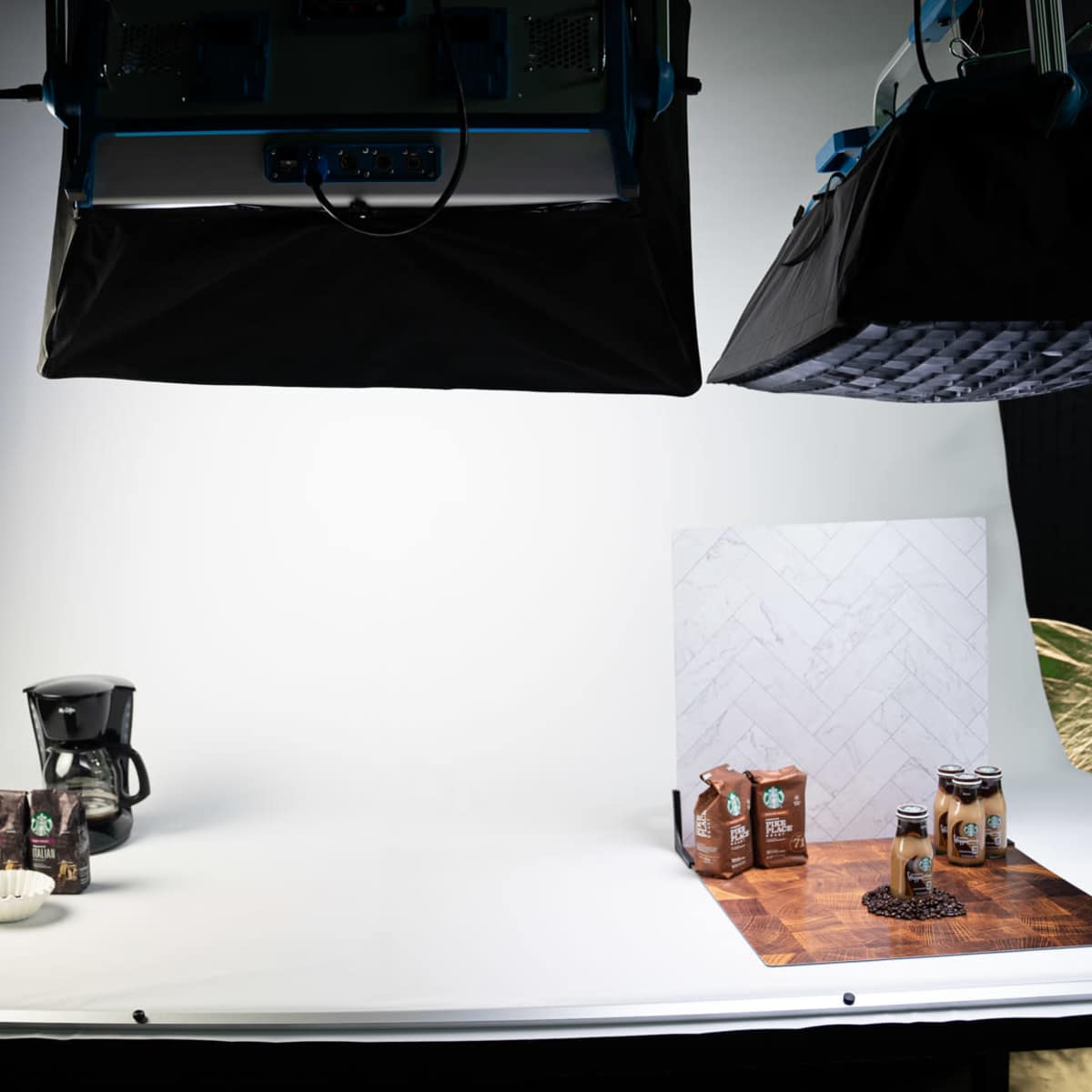 A photography studio setup with a coffee maker, coffee boxes, and cans arranged on a wooden surface against a white backdrop.