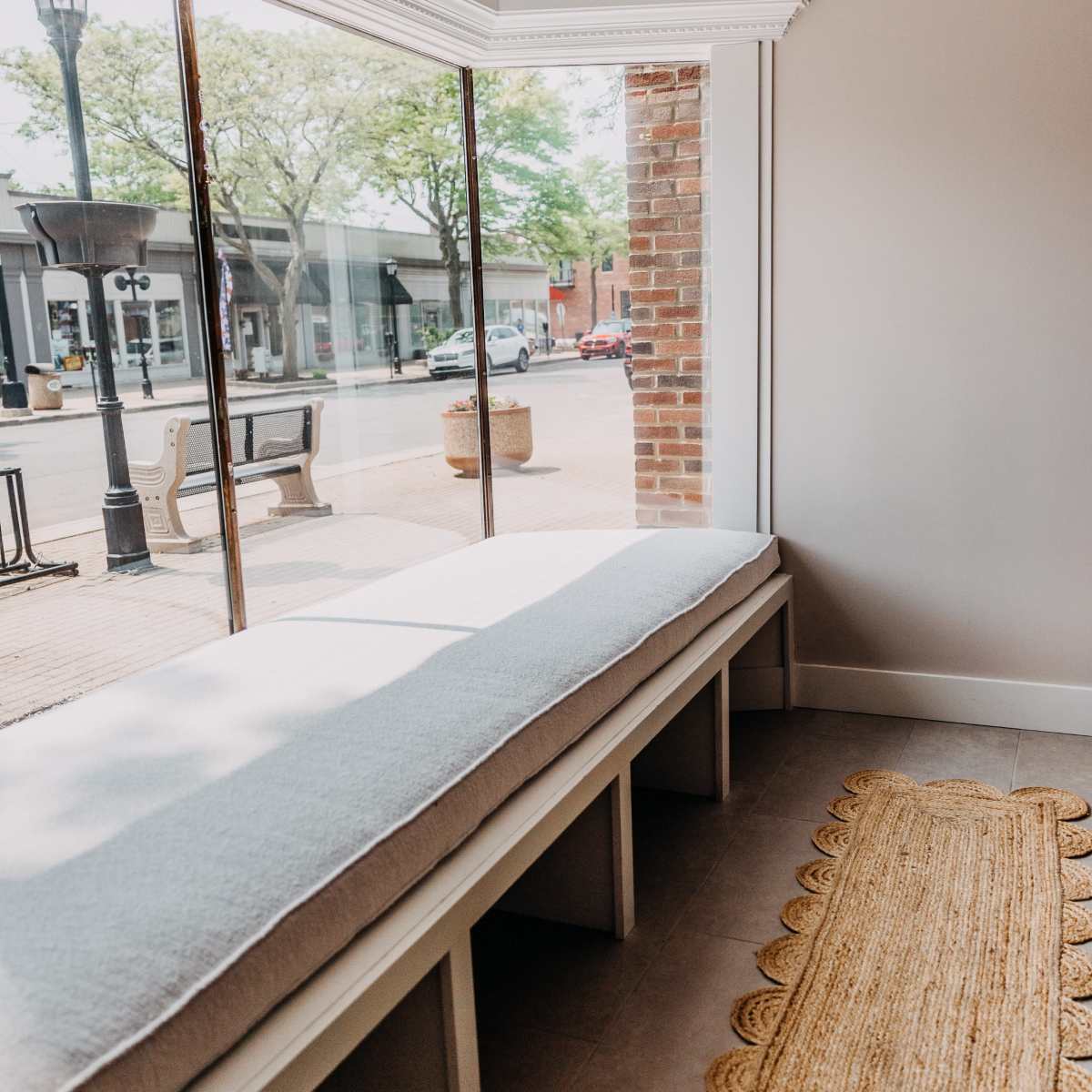 A cozy seating area with a long, cushioned bench by a large window and a woven rug on the floor.