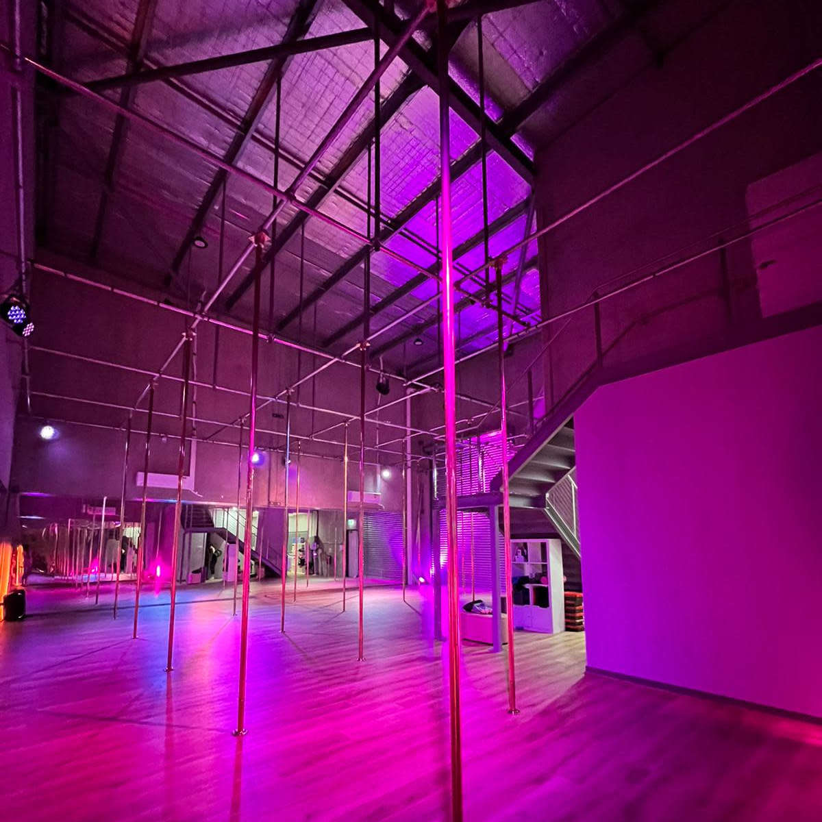 A spacious indoor area with framed poles and dim lighting in shades of pink and purple.
