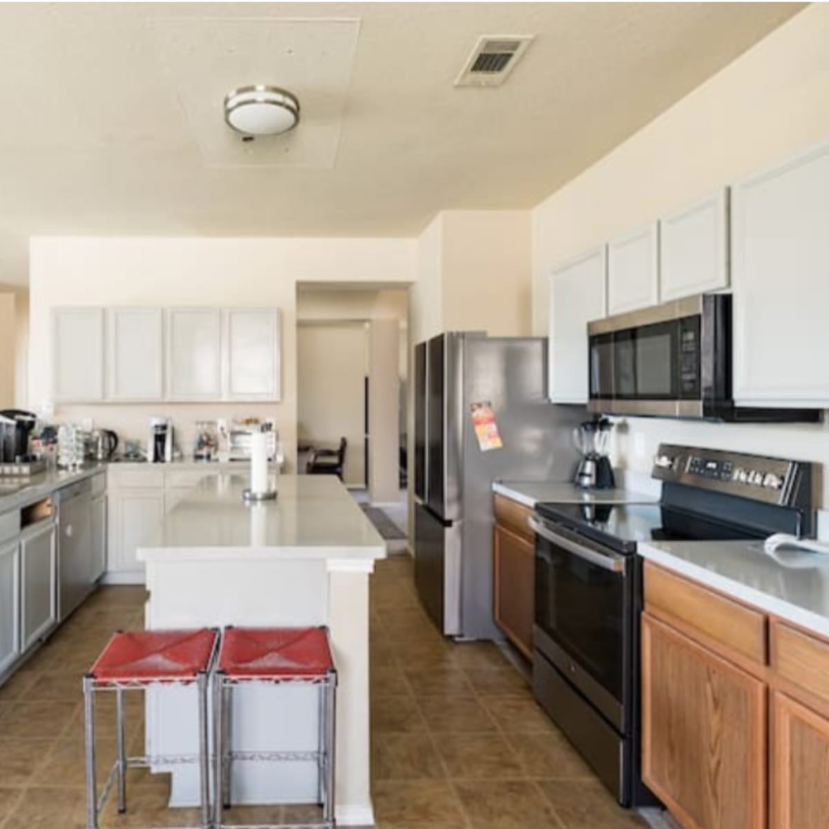 A spacious kitchen features gray cabinets, stainless steel appliances, and a central island with two red stools.