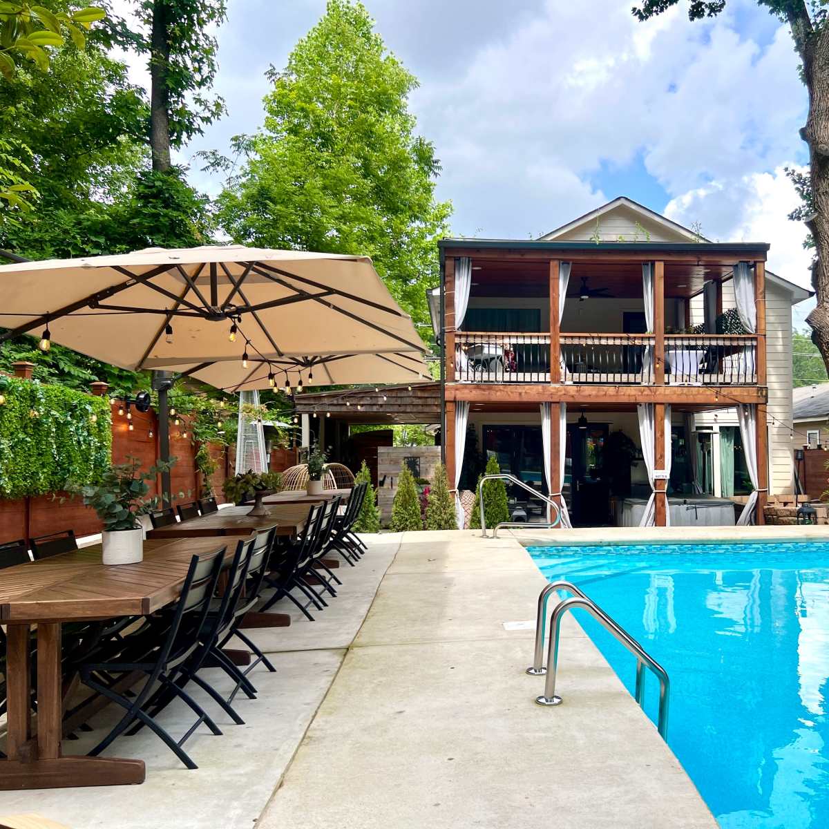 A backyard with a swimming pool, a large dining table, and a multi-level house surrounded by greenery.