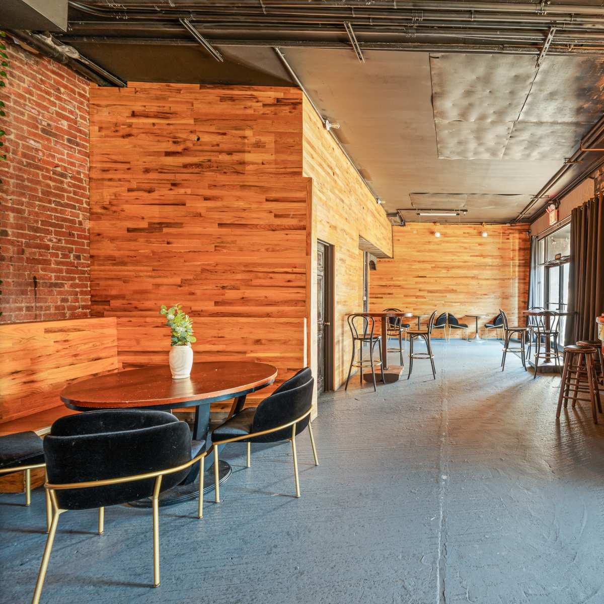 A spacious interior of a modern bar featuring wooden walls, a curved bar counter, and empty tables and chairs arranged around the room.