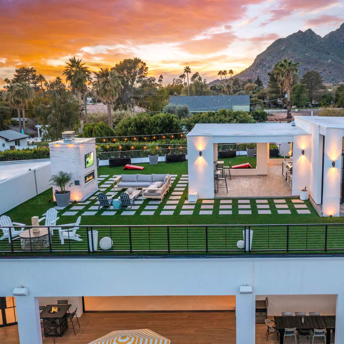 A rooftop terrace with landscaped grass, seating areas, and views of a mountainous landscape at sunset.