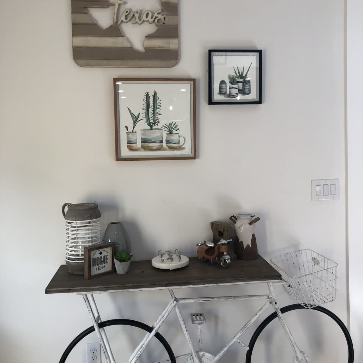 A wooden table with bicycle wheels displays various decorative items, surrounded by framed art on the wall, including a Texas sign.
