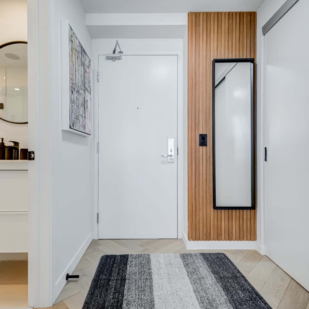 A modern entryway featuring a white door, a round mirror on the wall, and a striped rug on a light wooden floor.