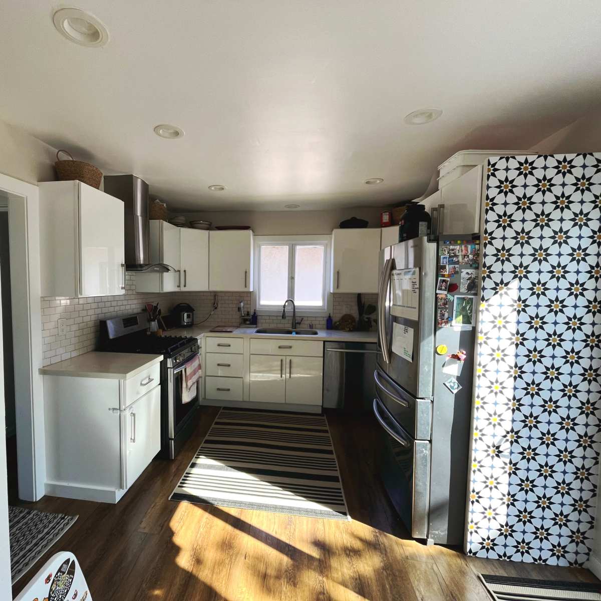 A bright kitchen features white cabinets, a stainless steel refrigerator, and a striped rug on the floor.