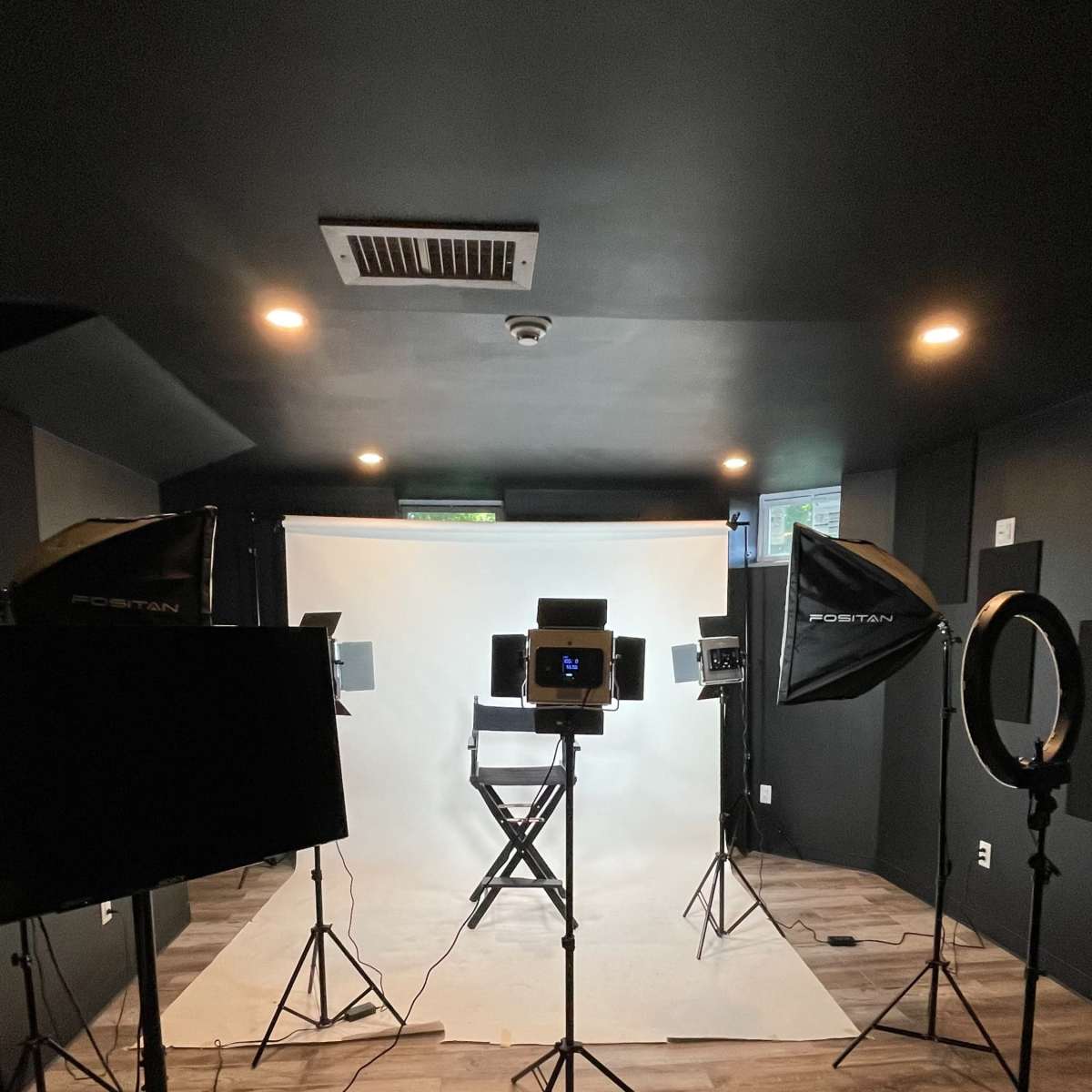 A photography studio set up with lighting equipment, a white backdrop, and a director's chair.
