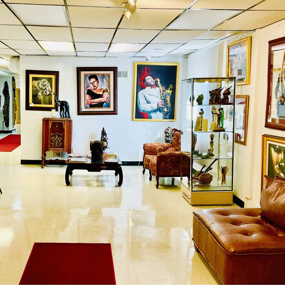 An art gallery with framed paintings and sculptures displayed on the walls and a brown leather couch in the foreground.
