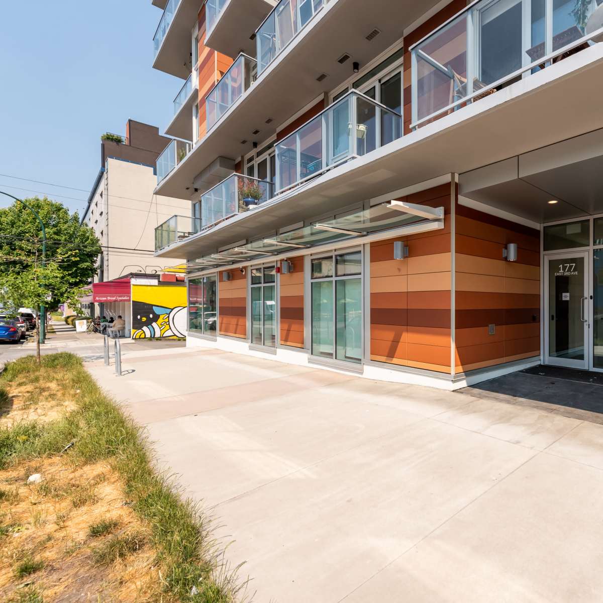 The entrance of a modern building with orange and gray paneling, featuring large glass windows and a bike parked outside.