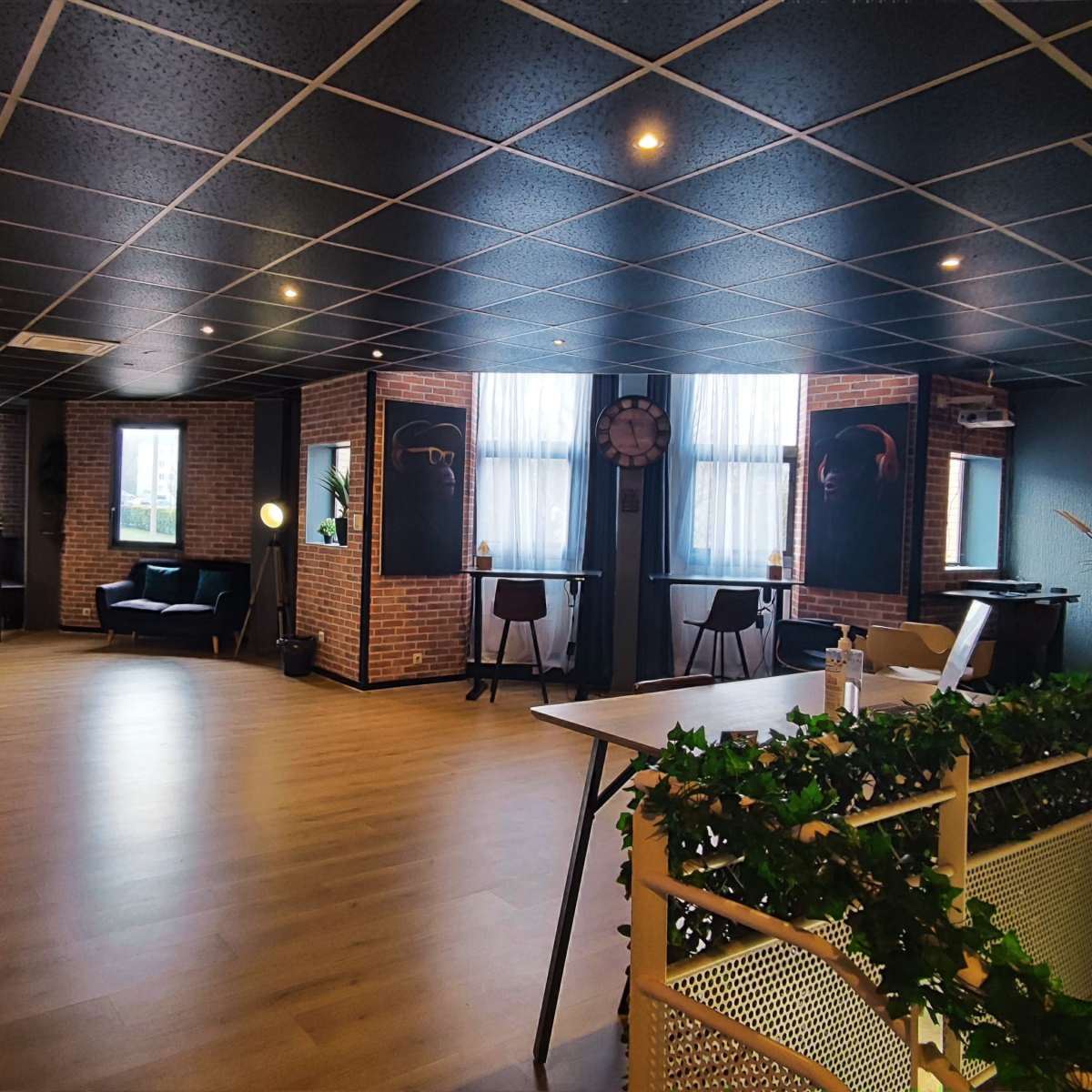 A spacious office interior with a reception area, seating arrangements, large windows, and a table decorated with greenery.