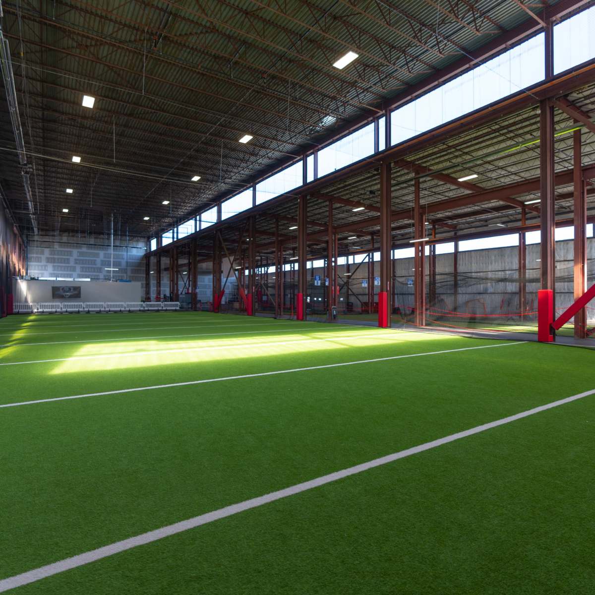 An indoor sports facility with artificial turf, featuring open spaces and large windows along the walls.