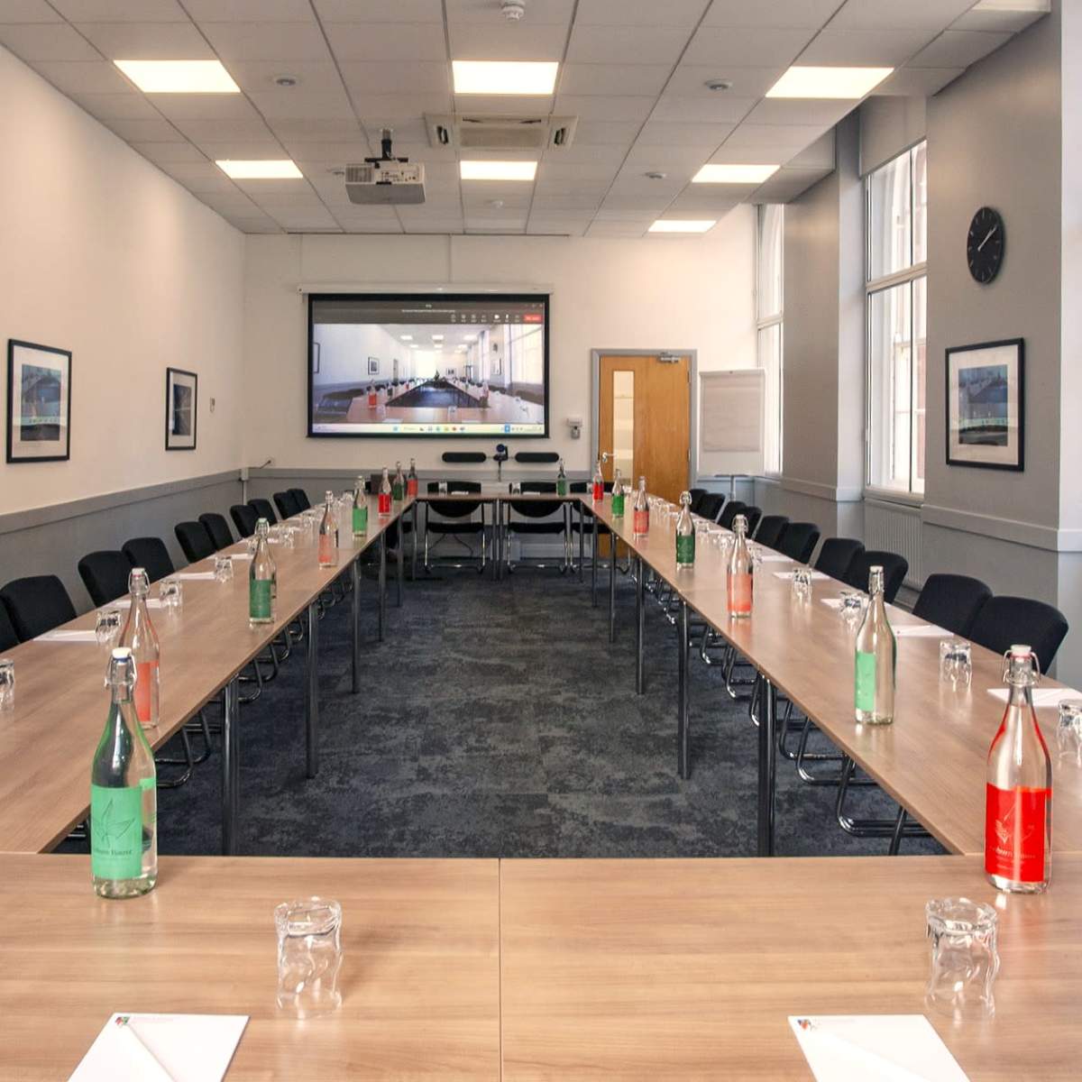 A conference room is arranged with a long table, chairs on either side, and bottles of water in various colors on the table.
