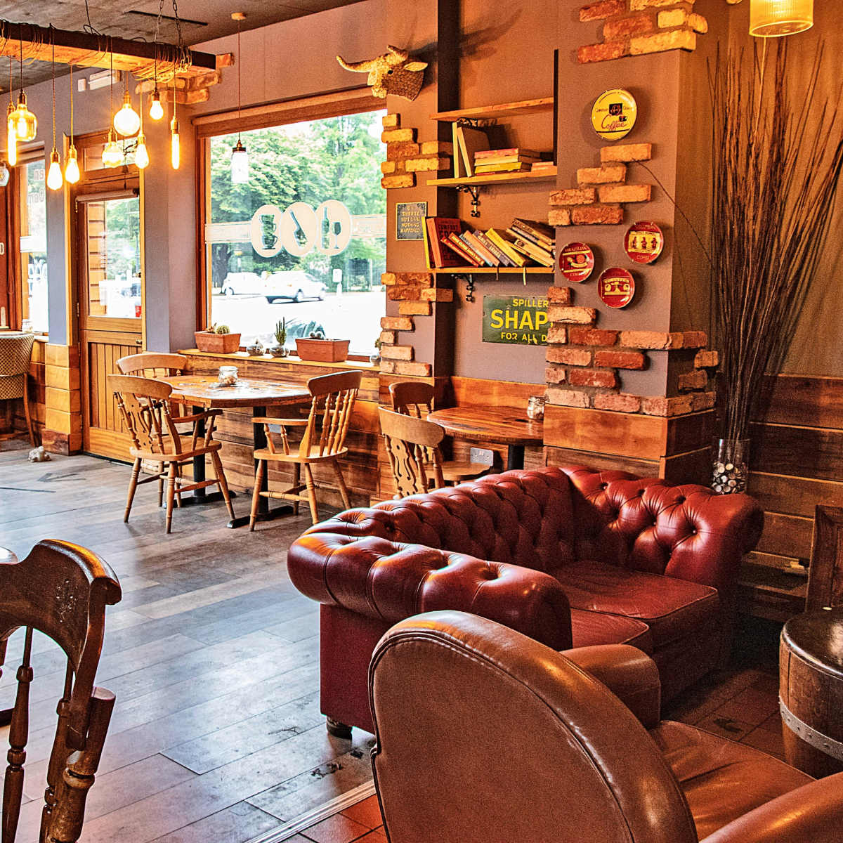 A cozy café interior with wooden tables and chairs, exposed brick walls, and large windows allowing natural light to enter.