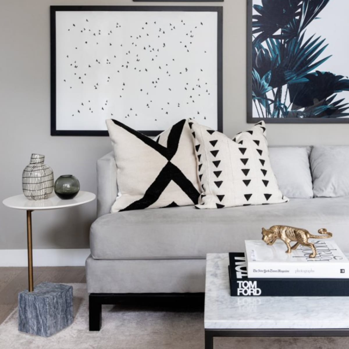 A modern living room corner with a gray couch adorned with patterned pillows, a marble coffee table, and framed art on the wall.