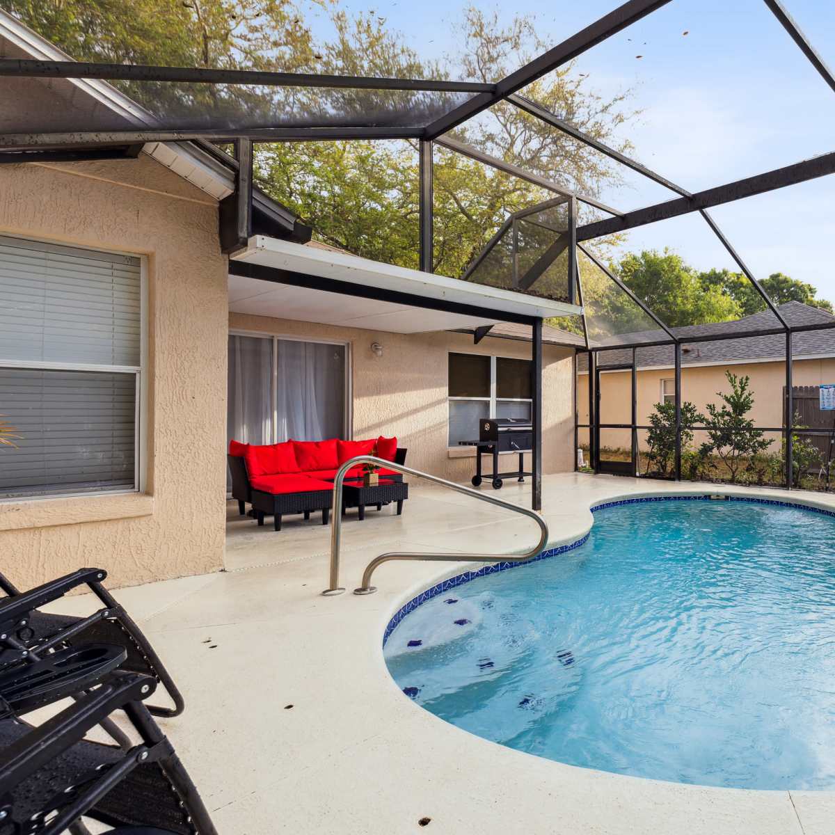A screened-in backyard pool area with a small round swimming pool, patio furniture, and surrounding greenery.