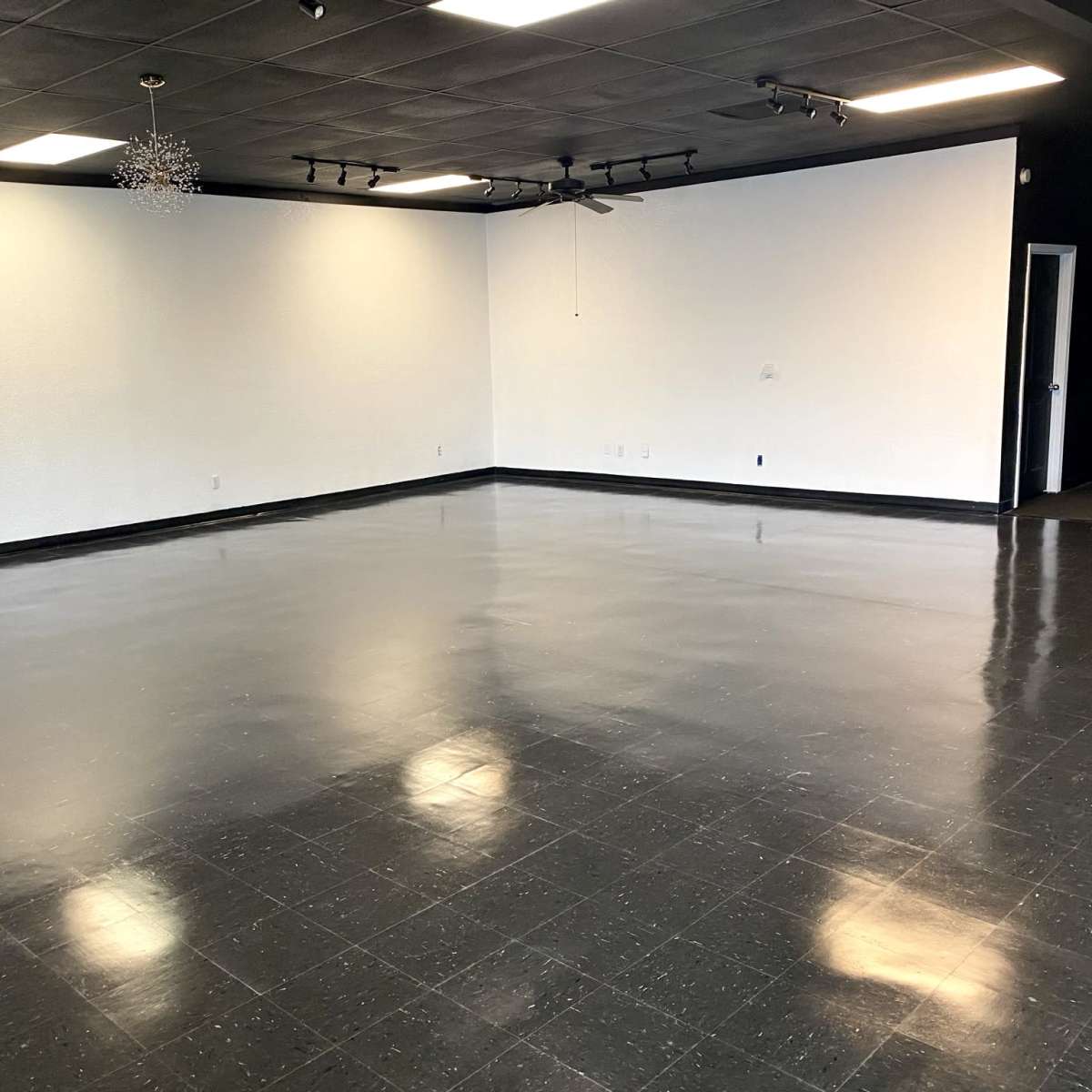 A spacious, empty room with a shiny black floor and white walls, illuminated by ceiling lights.